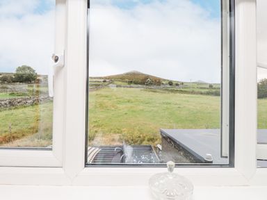 A view of a grassy field with stone walls and a hill in the background seen through a white window frame