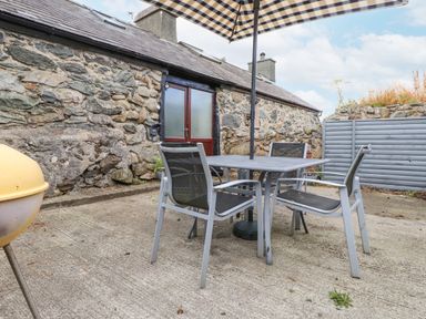 An outdoor patio area with a stone wall a metal table and chairs and a large umbrella at Quarry Cottage in Bethesda