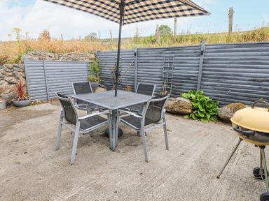 An outdoor patio with a table and chairs under a striped umbrella and a barbecue grill at Quarry Cottage in Bethesda