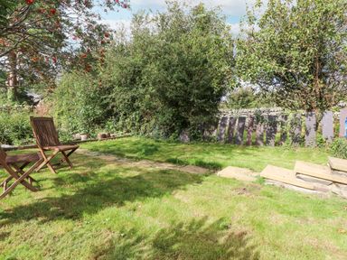 A garden with two wooden chairs a stone pathway green grass and trees at Quarry Cottage in Bethesda