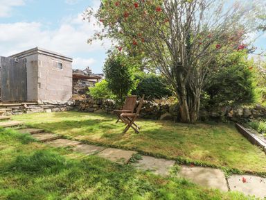 A garden with a tree a wooden chair stone steps and a small stone shed at Quarry Cottage in Bethesda