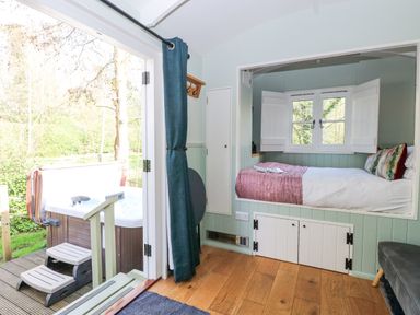 A small room with a bed built into the wall with windows above and a hot tub outside on a wooden deck at Damsel Shepherds Hut in Badwell Ash