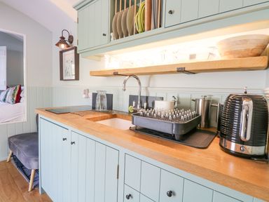 A kitchen countertop with a sink dish rack kettle and wooden cabinets at Damsel Shepherds Hut in Badwell Ash