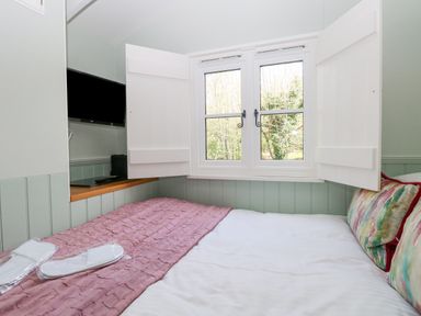 A bedroom with a bed, window with shutters, mounted television, and pillows at Damsel Shepherds Hut in Badwell Ash