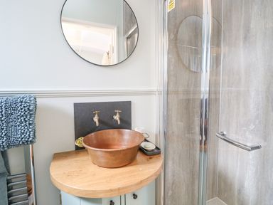 A bathroom with a round mirror above a copper basin on a wooden countertop next to a glass shower at Damsel Shepherds Hut in Badwell Ash