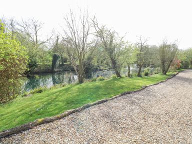 A gravel path next to a grassy area and a pond with trees at Damsel Shepherds Hut in Badwell Ash