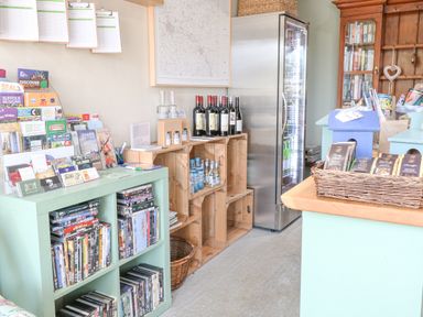 A room with bookshelves containing DVDs pamphlets wine bottles and a refrigerated display at Damsel Shepherds Hut Badwell Ash