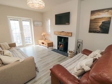 A living room with a beige sofa and a brown leather sofa facing a fireplace with a wood stove and a wall-mounted TV at Ocean Spray in Scarborough