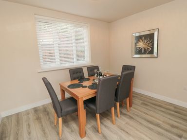 A dining room with a wooden table and six upholstered chairs near a window with blinds at Ocean Spray in Scarborough