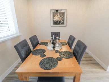 A dining room with a wooden table six gray chairs placemats and a tray with wine glasses and a bottle at Ocean Spray in Scarborough