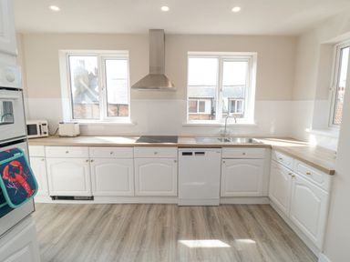 A kitchen with white cabinets wooden countertops a stainless steel sink two windows and appliances at Ocean Spray in Scarborough