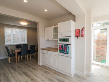 A kitchen with white cabinetry and built-in oven next to a dining area with a wooden table and black chairs at Ocean Spray in Scarborough