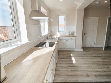 A kitchen with wooden countertops white cabinets a stove sink kettle and windows at Ocean Spray in Scarborough