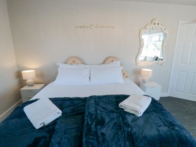 A bedroom with a double bed two bedside tables with lamps a decorative mirror and folded towels on a blanket at Ocean Spray in Scarborough