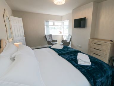 A bedroom with a bed towels two chairs a wall-mounted tv and a chest of drawers at Ocean Spray in Scarborough
