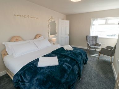 A bedroom with a large bed with white bedding and a blue blanket two gray chairs near a window and a mirror on the wall at Ocean Spray in Scarborough