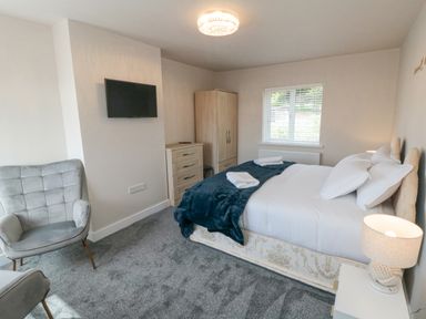 A bedroom with a double bed two folded towels a gray armchair a chest of drawers a wardrobe a wall-mounted TV and a bedside lamp at Ocean Spray in Scarborough