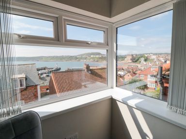 A corner window with a view of rooftops and a coastal town with a beach and a ferris wheel at Ocean Spray in Scarborough