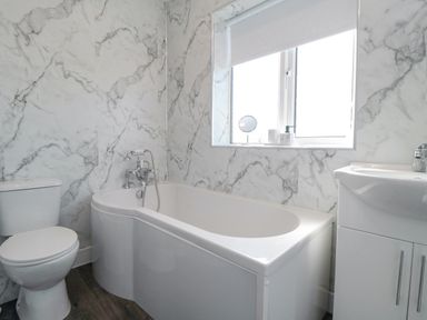 A bathroom with a white toilet a bathtub under a window and a sink with cabinet at Ocean Spray in Scarborough