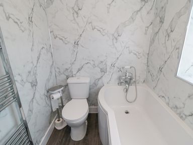 A bathroom with a toilet next to a bathtub and a towel rack on the wall at Ocean Spray in Scarborough