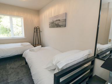 A bedroom with two single beds a window a wall-mounted photo a clothes rack and a mirror at Ocean Spray in Scarborough