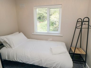 A bedroom with a single bed with white bedding next to a window and a black clothes rack with hangers at Ocean Spray in Scarborough