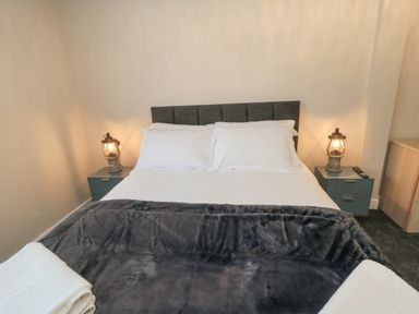 A bedroom with a double bed white pillows a dark headboard two bedside tables with lamps and a folded towel at Ocean Spray in Scarborough