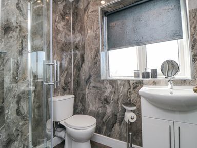 A bathroom with a toilet a sink window with a roller blind and a glass shower enclosure at Ocean Spray in Scarborough