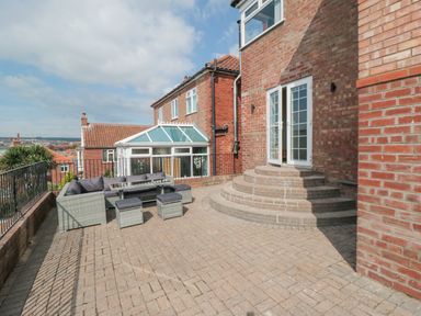 A brick patio with outdoor seating and steps leading to white double doors at Ocean Spray in Scarborough