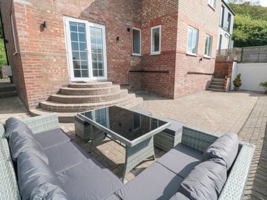 A patio area with outdoor wicker furniture and glass table outside a brick building at Ocean Spray in Scarborough