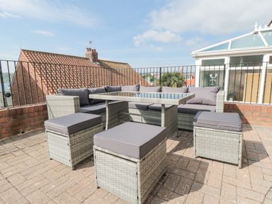An outdoor patio area with grey cushioned wicker seating and glass-top table at Ocean Spray in Scarborough