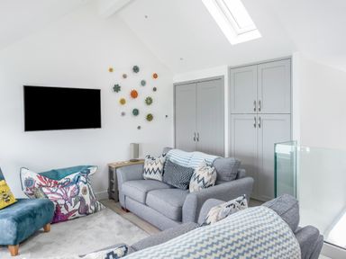 A living room with grey sofas, patterned cushions, a wall mounted TV, decorative wall art, and grey cabinets at Loe Cottage in Porthleven