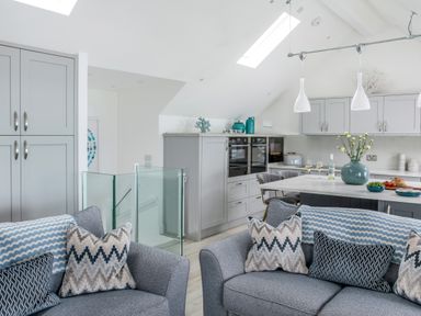 A kitchen and living area with grey sofas with patterned cushions and a kitchen island with flowers at Loe Cottage in Porthleven