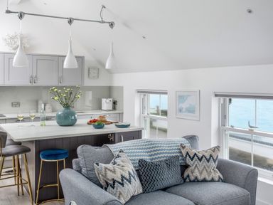 A kitchen and living area with a blue sofa with patterned cushions and a kitchen island with bar stools at Loe Cottage in Porthleven