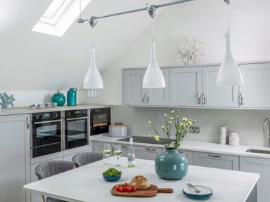 A kitchen with gray cabinets, a white countertop island, two gray chairs, a blue vase with flowers, and kitchen appliances at Loe Cottage in Porthleven