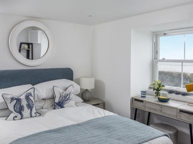 A bedroom with a bed a bedside table with a lamp a desk by a window and pillows with seahorse designs at Loe Cottage in Porthleven