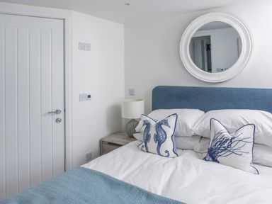 A bedroom with a white door bedside table lamp bed with blue headboard and pillows with sea creature designs at Loe Cottage in Porthleven