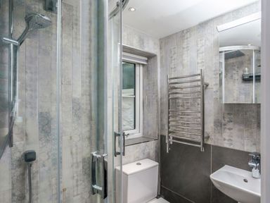 A bathroom with a shower, toilet, sink, heated towel rail, and window at Loe Cottage in Porthleven