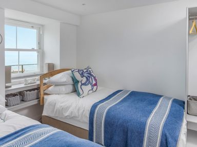 A bedroom with two single beds blue blankets pillows and a window with a view at Loe Cottage in Porthleven