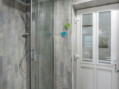 A shower with glass door and a white door with windows in a tiled bathroom at Loe Cottage in Porthleven