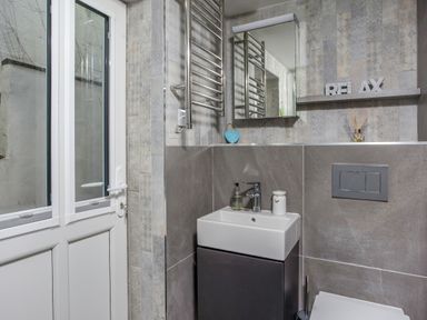 A bathroom with a small sink and mirror with a shelf above and a white door at Loe Cottage in Porthleven