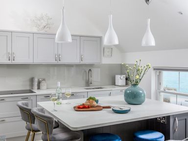 A kitchen with an island counter featuring a vase with flowers glasses with wine bread and tomatoes Loe Cottage in Porthleven