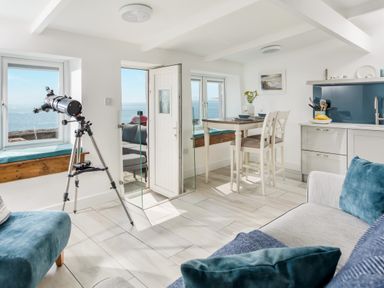 A room with a telescope near a window a dining table with two chairs and a kitchen area at Loe Cottage in Porthleven