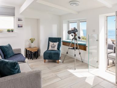 A living room with a telescope by the window and a chair with a pillow at Loe Cottage in Porthleven