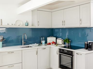 A kitchen with white cabinets a blue backsplash and a sink next to a stove with a toaster bread box and utensils at Loe Cottage in Porthleven