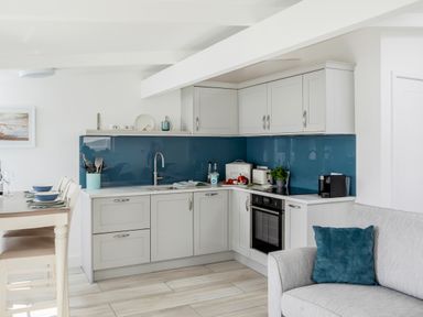 A kitchen with white cabinets blue backsplash and a dining table with chairs at Loe Cottage in Porthleven