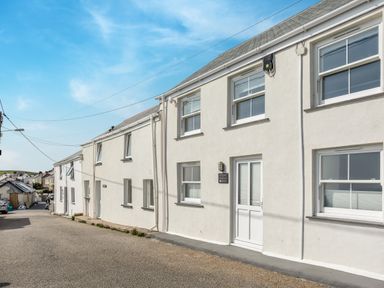 A row of white houses along a street with windows and doors under a clear blue sky at Loe Cottage in Porthleven