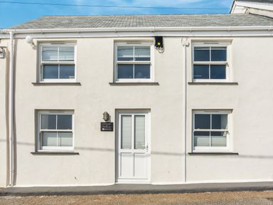 The exterior of a white two-story building with a door centered between four windows at Loe Cottage in Porthleven