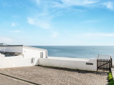 A paved parking area next to a white wall and gate overlooking the sea at Loe Cottage in Porthleven