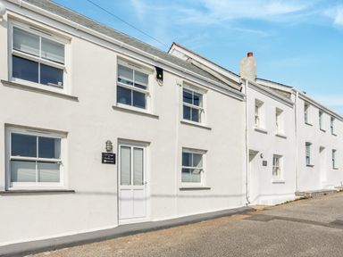 A row of white cottages with windows and doors on a paved street at Loe Cottage in Porthleven